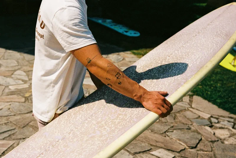 Tattooed forearm resting on a white longboard on a stone terrace