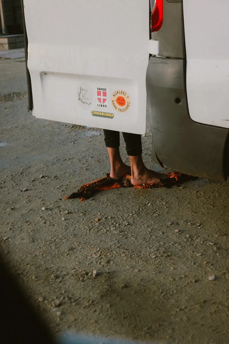Bare feet on an orange towel behind the open back door of a white van