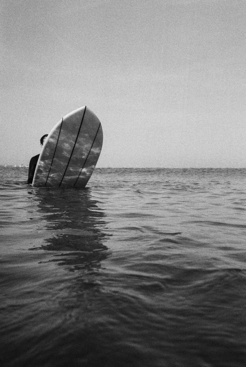 Black and white, the nose of a surfboard sticking out of flat water