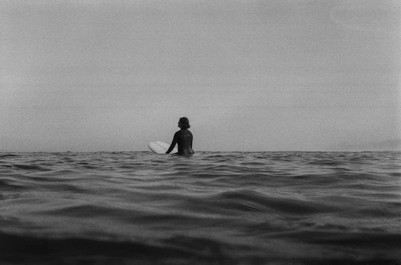 Black and white, a surfer sitting on a longboard, waiting on a flat sea