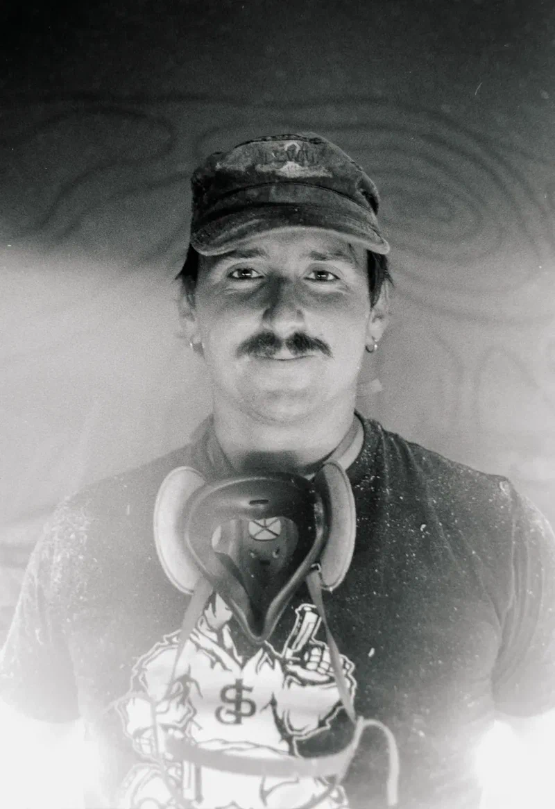 Black and white portrait of a man with a moustache and headphones around his neck
