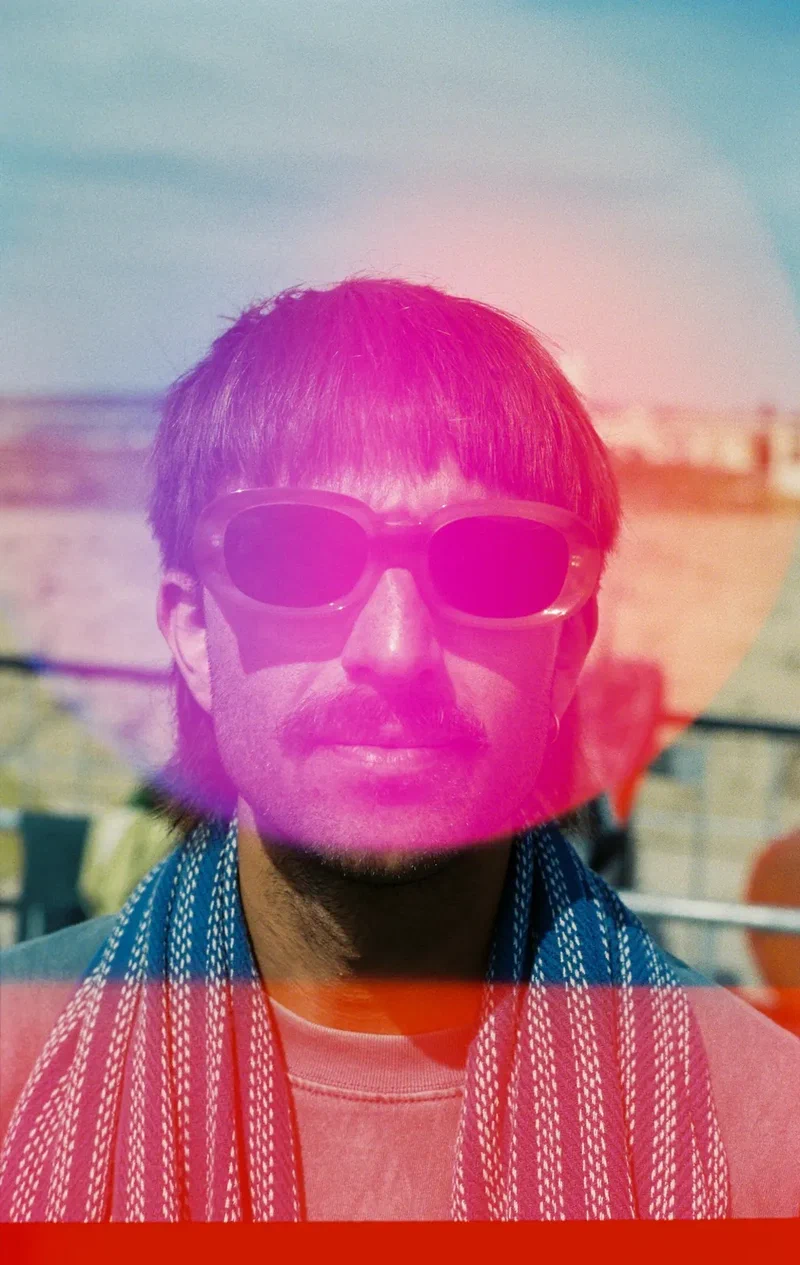Man in sunglasses with a towel on his shoulders, a pink light leak across his face