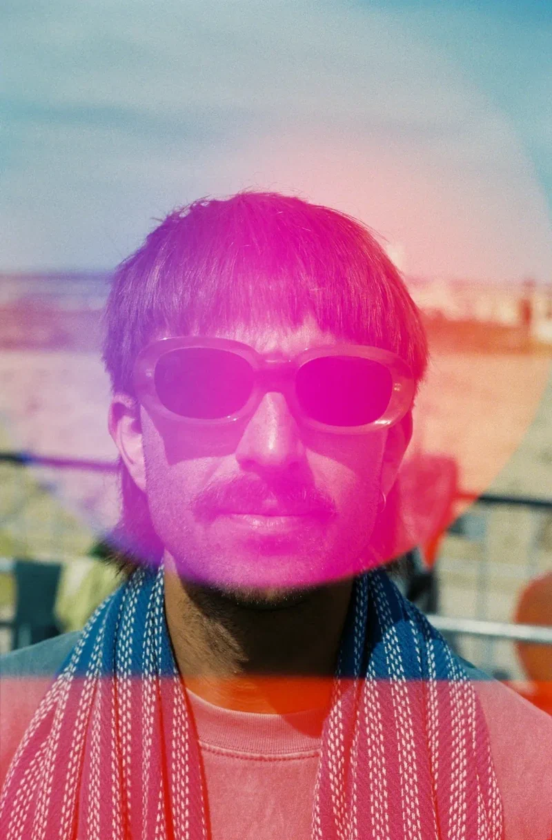 Man in sunglasses with a towel on his shoulders, a pink light leak across his face