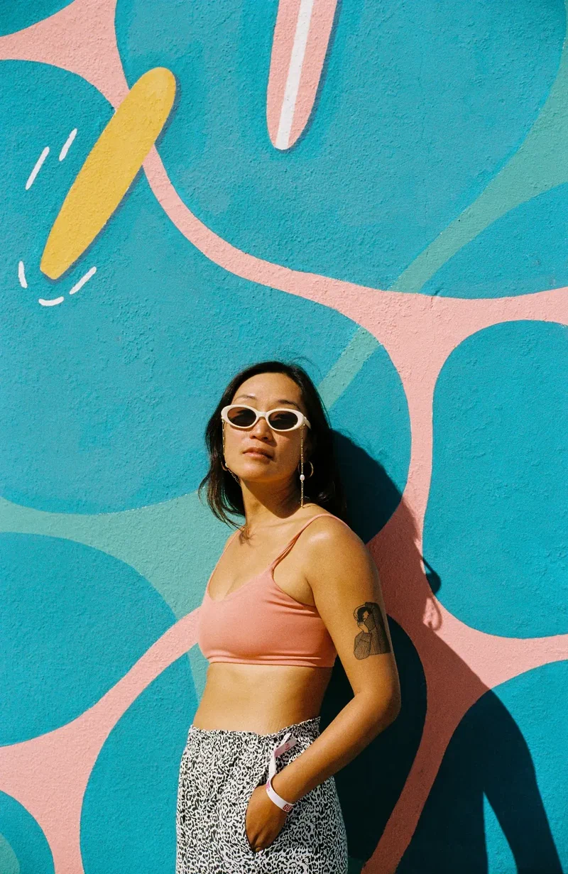 Woman in white sunglasses leaning against a blue and pink mural
