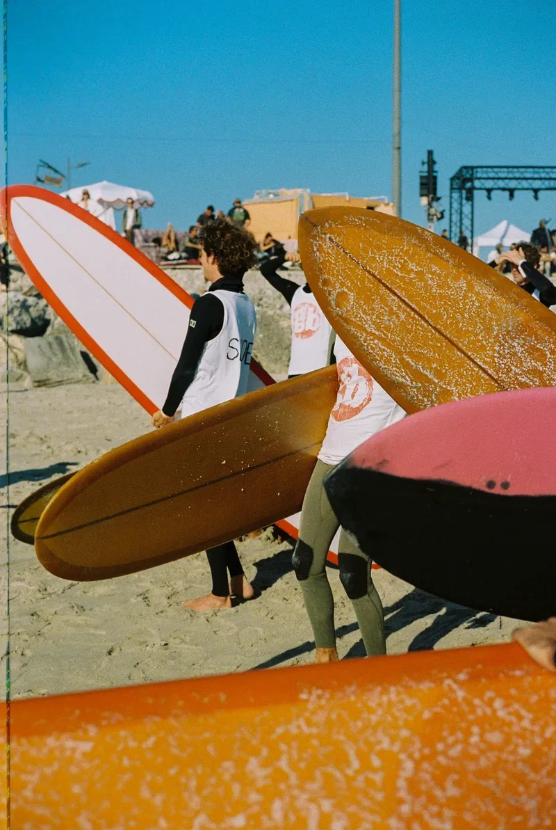 Surfers carrying longboards across a crowded beach