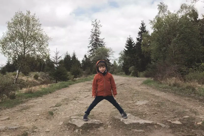 Enfant en manteau rouge, jambes écartées, sur un chemin de terre