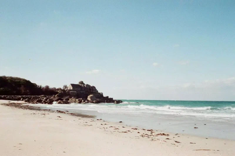 Plage de sable blanc et vagues turquoise au pied des rochers
