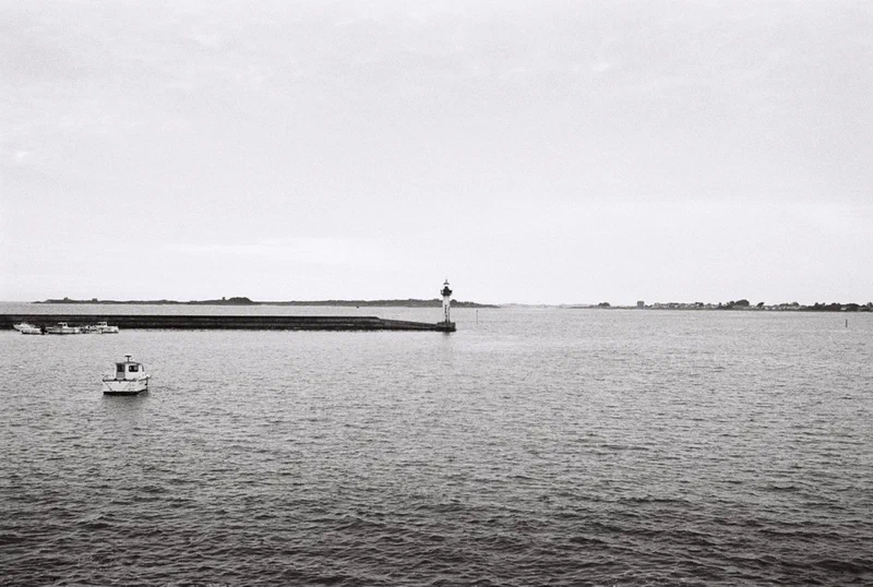 Entrée de port en noir et blanc, phare et petit bateau