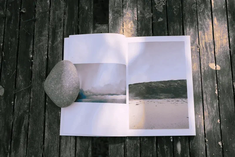 Le zine A Thousand Tides ouvert sur un ponton en bois, un galet posé dessus