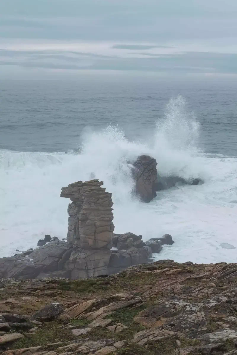Vague qui explose derrière une aiguille de roche sur la côte sauvage
