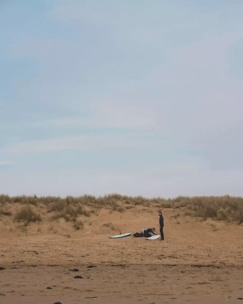 Surfeur qui prépare sa planche au pied des dunes