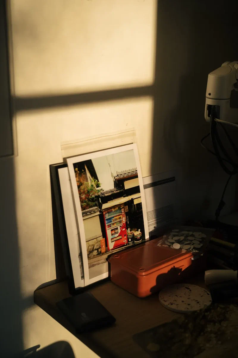 Afternoon light on a desk with framed prints and an orange box
