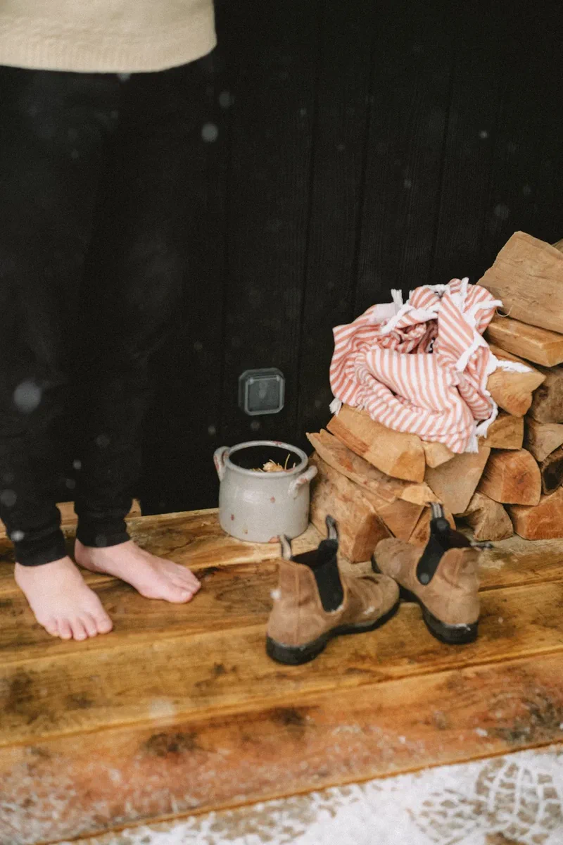 Bare feet, boots and a pile of firewood on the porch