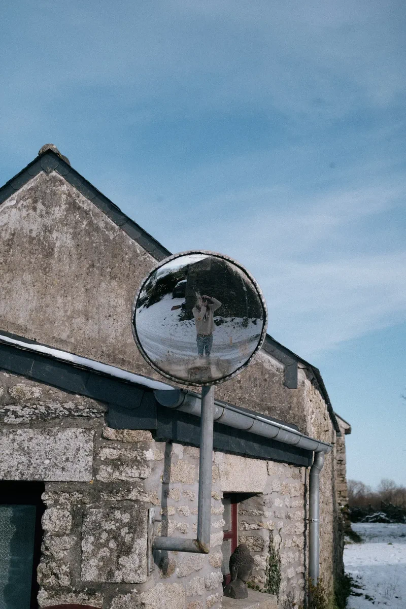 Road mirror on an old stone barn after the snow