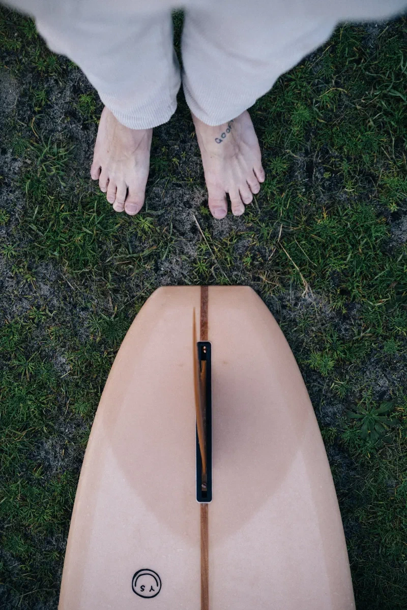 Bare feet in the grass above a peach-coloured surfboard