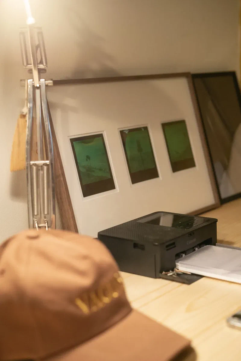Polaroid prints framed above a printer, a cap in the foreground