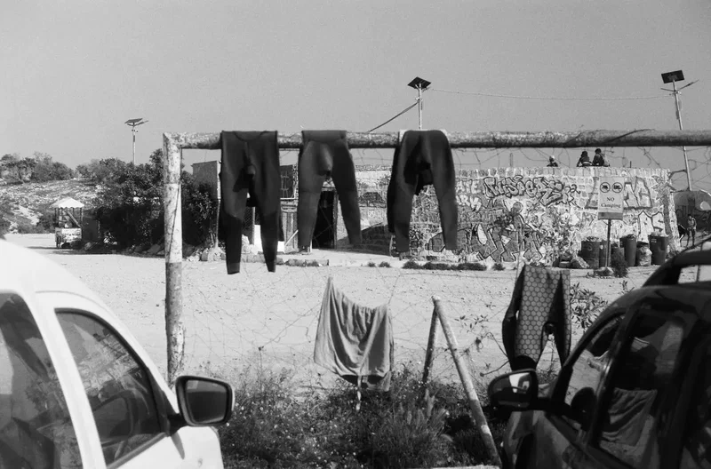 Wetsuits drying on a fence above a busy beach, black and white