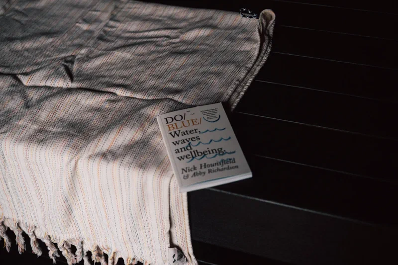 Striped towel and a book on water and wellbeing on a bench