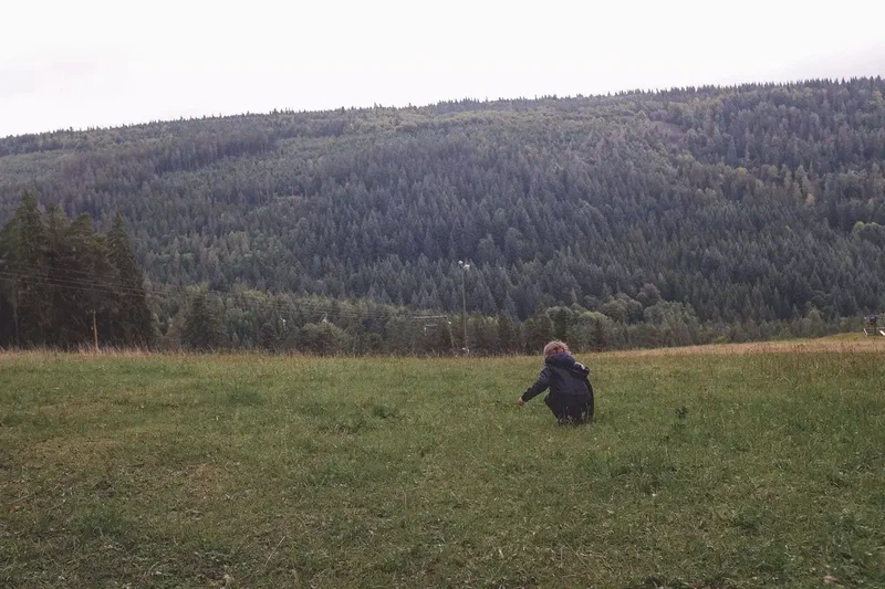 Enfant accroupi dans une prairie devant une colline boisée