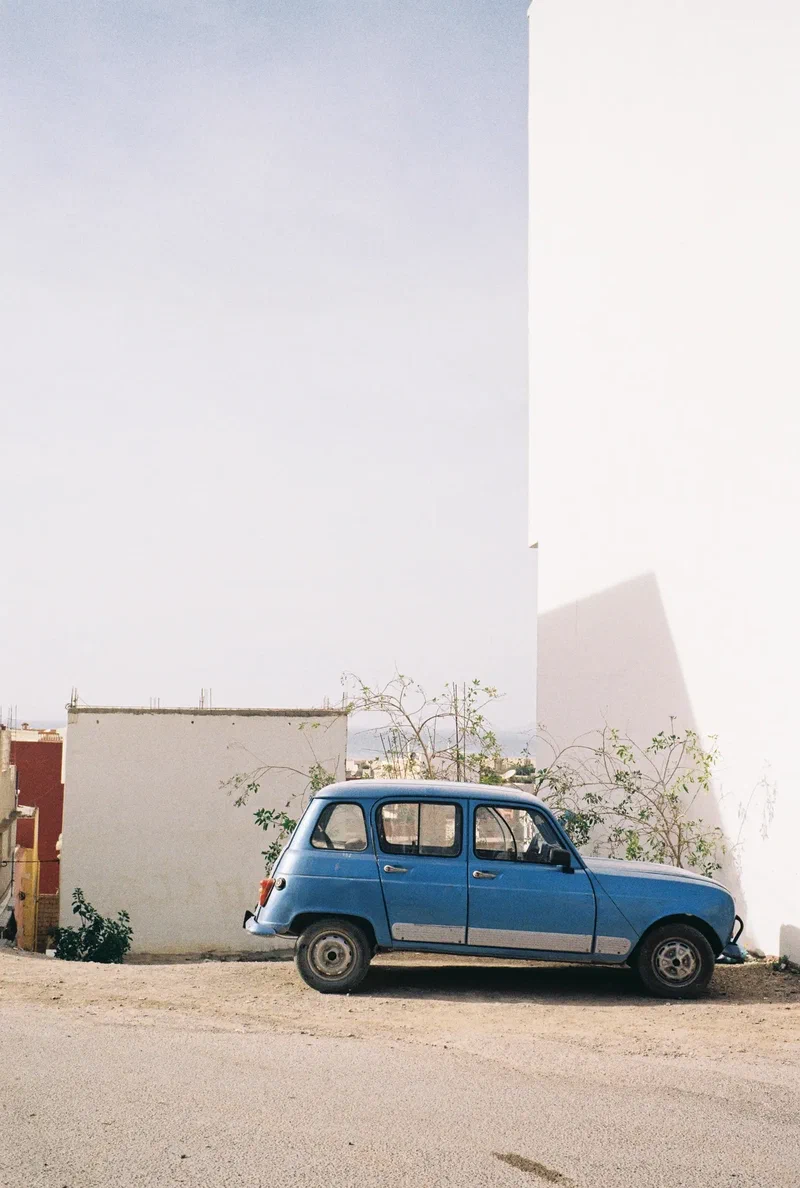Renault 4 bleue garée devant un mur blanc