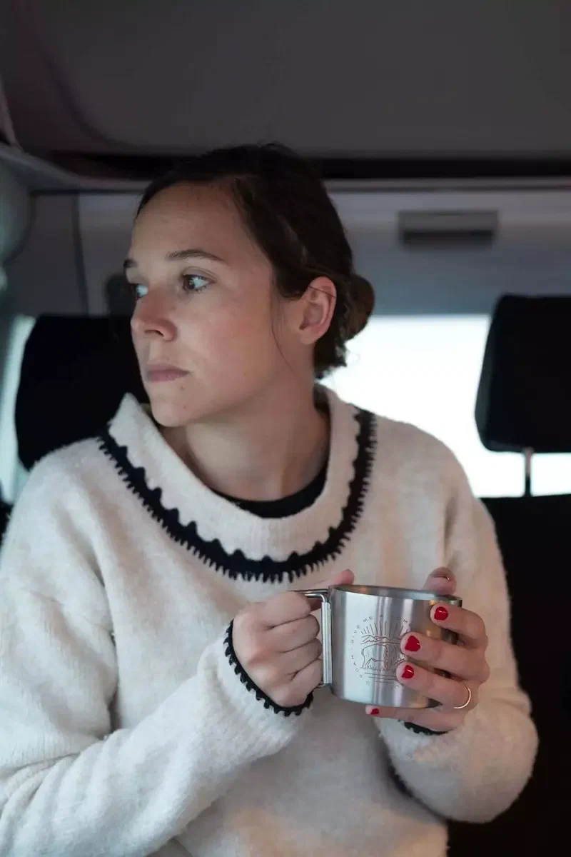 Femme en pull blanc qui boit dans une tasse en métal dans le van