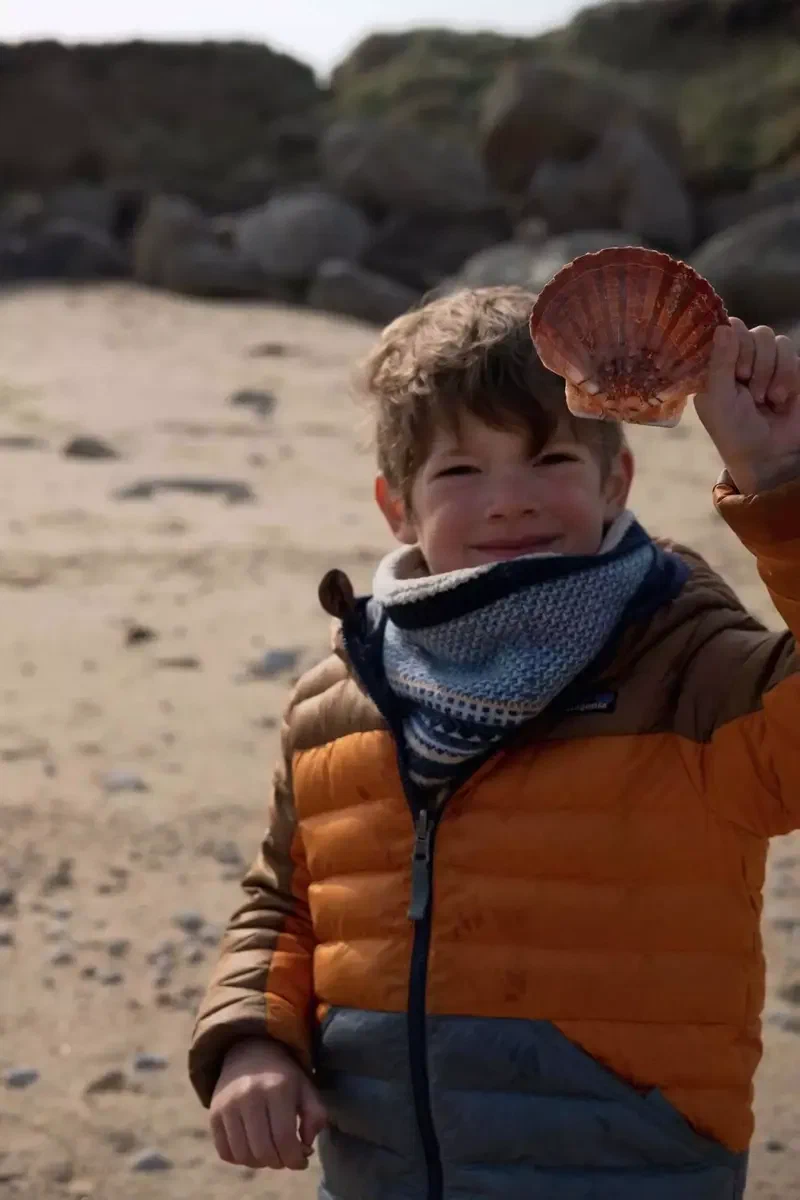 Enfant en doudoune orange qui tient une coquille Saint-Jacques