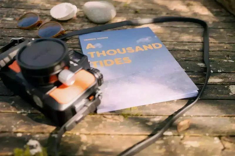 The A Thousand Tides zine next to a camera on a wooden table