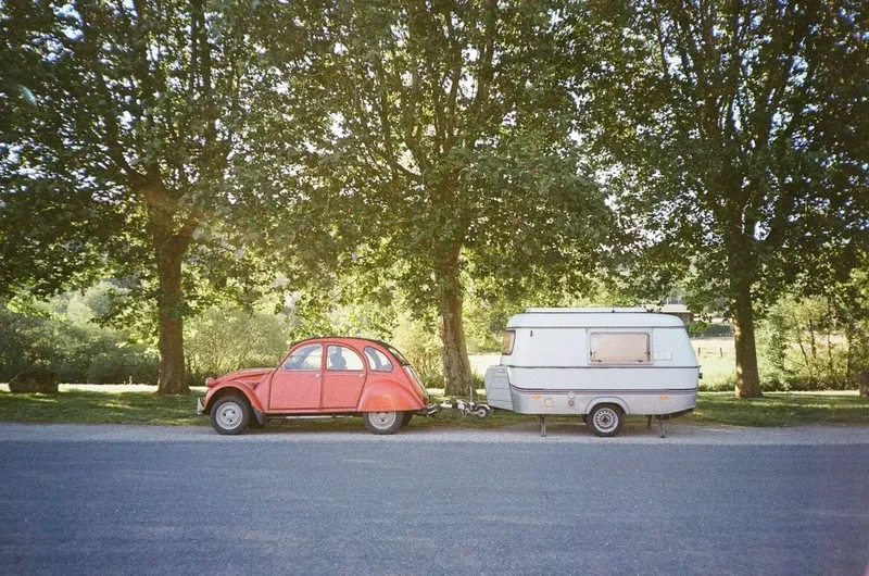 2CV rouge et caravane garées sous les arbres